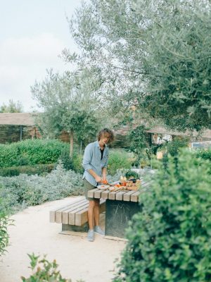 A man cuts vegetables on a wooden table in a lush outdoor garden setting.