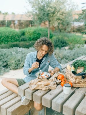A young man sitting at a picnic table, enjoying a fresh meal surrounded by greenery.