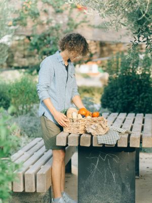 Person arranging fresh vegetables in a basket on a table in a garden setting.